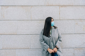 Portrait of a beautiful adult young woman against a gray wall in a medical face mask