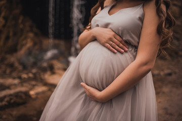 pregnant woman with a big belly in a white long dress in nature on the background of a waterfall