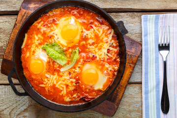 israeli fried eggs shakshuka with cheese in a frying pan next to a fork and a napkin.