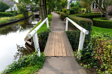Wooden decorative footbridge over a canal in the Netherlands in the background of plants and buildings.