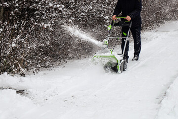 Human cleans snow off path with wireless electric snow blower after the winter snowfall