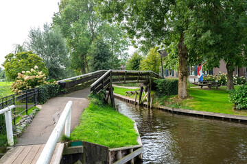 Fototapeta na wymiar Wooden decorative footbridge over a canal in the Netherlands in the background of plants and buildings.