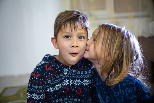 Two siblings in pajamas with book, sister kiss brother, funny emotions huge home