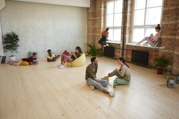 Group of young dancers relaxing after sports training they listening to music and using mobile phones in dance studio