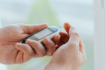 diabetes, healthcare - close up of a man with a glucometer and a test strip checking blood sugar at home