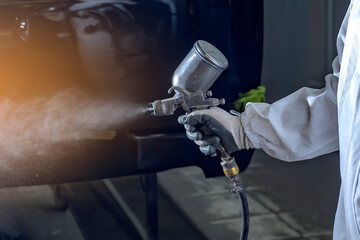 automobile repairman painter in protective workwear and respirator painting car body in paint...