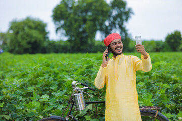 Young indian farmer talking on mobile phone and showing money at cotton field