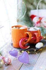 Two cups of coffee with meringues, caramel, Christmas decorations, hearts, illumination on a wooden windowsill, the concept of home comfort, love, winter holidays