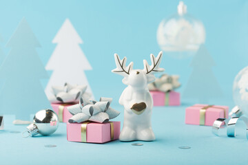 Christmas card with pink Xmas gifts, small glass white deer, silver decorations, mirror disco balls on light blue background.