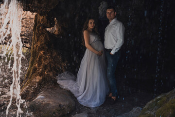 Fototapeta na wymiar Family couple a man with a pregnant woman with a big belly in nature on the background of a waterfall.