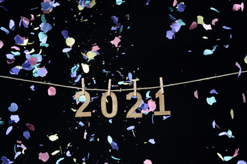 Año nuevo de 2021 en números de madera dorada colgados de una cuerda con pinzas de oficina sobre fondo negro y confeti cayendo