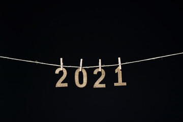 Año nuevo de 2021 en números de madera dorada colgados de una cuerda con pinzas de oficina sobre fondo negro - obrazy, fototapety, plakaty