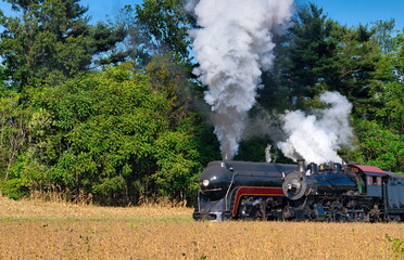Close up of an 2 Antique Steam Freight Train Puffing Smoke and Steam While going Thru Amish Countryside
