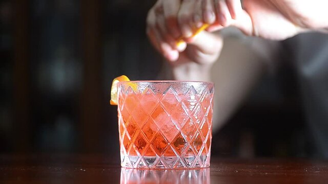 bartender squeezes orange rind into a glass with a Negroni cocktail
