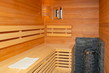 Compact sauna interior. Empty sauna wellness. Stones in a metal mesh inside the sauna. Steam room for wellness treatments. Classic steam room interior. Wooden walls and bench, stoun heaters.