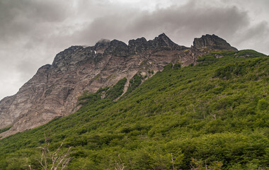 Ushuaia, Tierra del Fuego, Argentina - December 13, 2008: Martial Mountains in Nature Reserve. Brown mountain peaks rising into brown cloudscape. Lower part of flanks covered by green foliage.