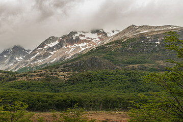 Ushuaia, Tierra del Fuego, Argentina - December 13, 2008: Martial Mountains in Nature Reserve. Brown snow covered mountain peaks rising into brown cloudscape. Green forest in front.
