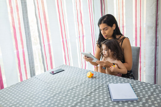 woman sitting with her baby daughter on her lap. holding a tablet while being watched and used