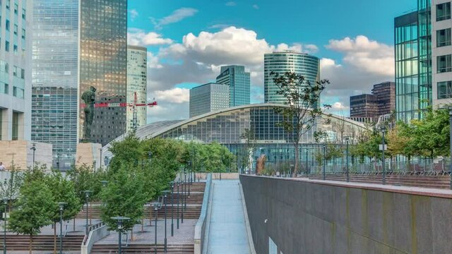 Skyscrapers of Defense modern business and financial district in Paris timelapse with highrise buildings. Green trees, blue cloudy sky in summer day. Reflections in modern towers.