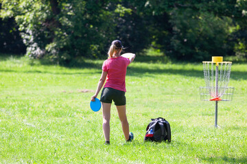 Young woman playing flying disc golf sport game in the city park or nature