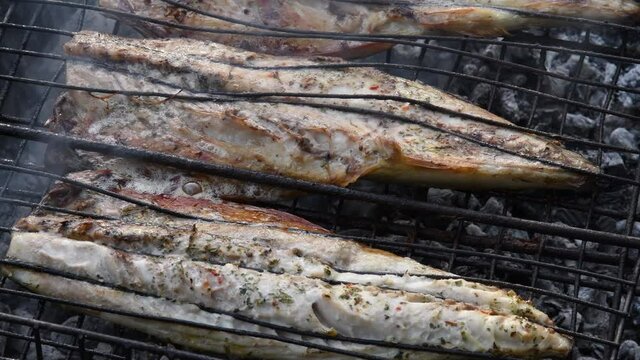 Juicy grilled mackerel fish inside grill grid on charcoal brazier with rising smoke. Fish preparation using outdoor barbecue grill