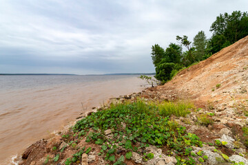 High bank of red clay and muddy water of the Volga river bay on a cloudy day.