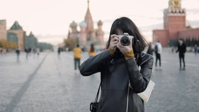 Young woman photographer at the centre of Red Square in Moscow. Handheld shot of happy young asian woman tourist taking pictures looking at the camera, handheld shot