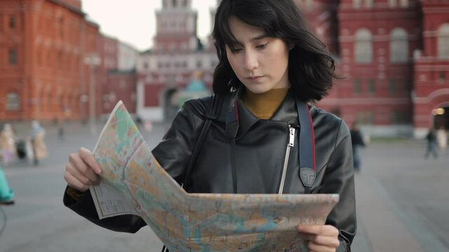 Young asian woman closeup with map on red square, tourist in Moscow. Black hair asian girl traveler with photo camera looking for a way in the centre of a big city, handheld shot