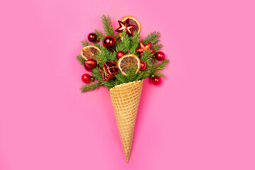 Ice cream cone with twigs of Christmas tree and toys on a pink background. New Year. Christmas card. Flat lay. The concept photo is an original Christmas present.