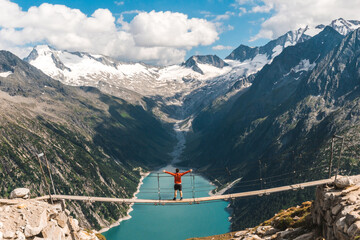 Man in a red tshirtjacket sitting on a suspension bridge above the Alps. Freedom and adventure concept. Touristic activities in Austrian Alps, Europe