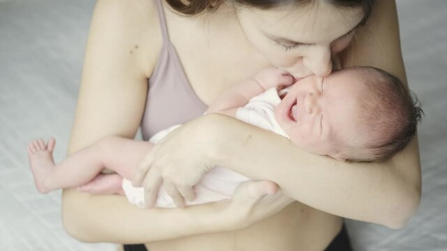 Portrait of a young mother and newborn baby. A young woman holds her little daughter in her arms and kisses her. Maternal love of new parents