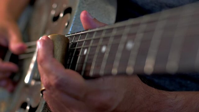 Man Playing Old Metallic Resonator Guitar with Slide Close Up Neck Shallow Focus