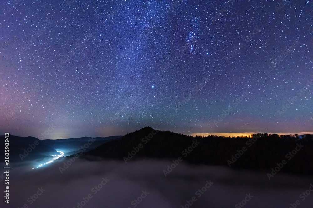 Wall mural a beautiful starry night in the mountains on top with beautiful scenery and fog.