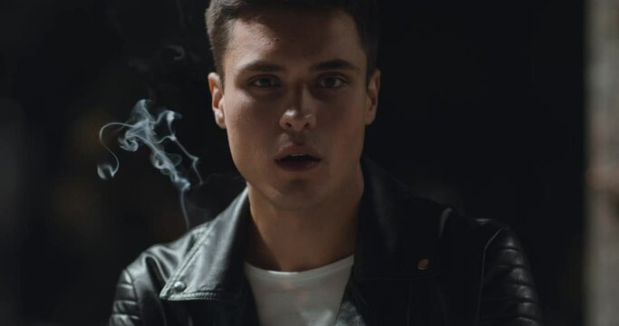 Outdoor portrait of serious man smoking at night park, slow motion