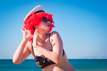 Close up portrait of a crazy middle aged lady in red wig, black shiny swimsuit eavesdrops against...