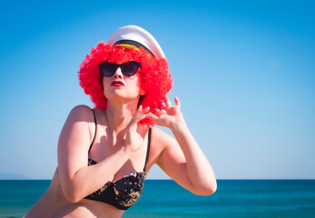 Close up portrait of a crazy middle aged lady in red wig, black shiny swimsuit eavesdrops against...