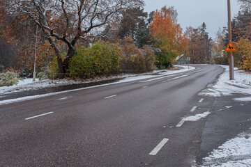 Scenic autumn view with first snow on the road, trees and forest in snow and hoarfrost against a cloudy sky background