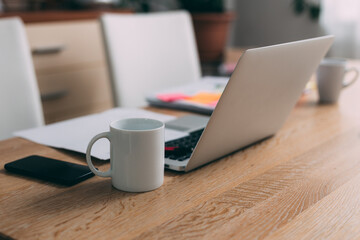 Busy desk for two workers  with laptop, phone, paperwork and cup of coffees. Work from home concept.