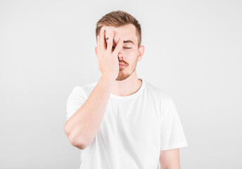 Fototapeta premium Worried American man covering face with both hands, looking at camera through his fingers