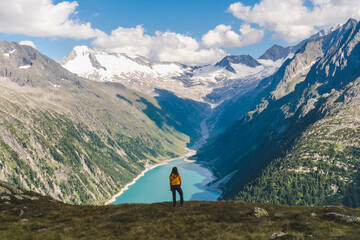 Young backpacker boy with the back at the camera watching a beautiful view over a lake in the Alps, scenic mountains in the background