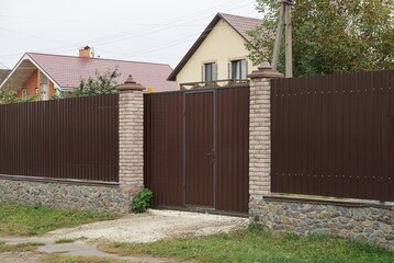 Fototapeta na wymiar brown metal gate and part of the wall of the fence made of wooden boards and bricks on the street