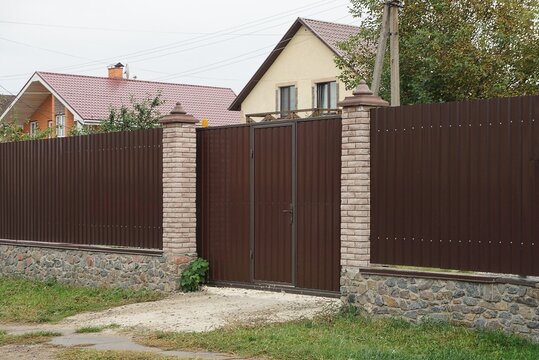  brown metal gate and part of the wall of the fence made of wooden boards and bricks on the street