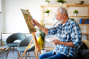 Smiling mature man painting on canvas at home