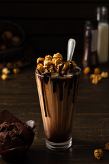 Tall glass cup with chocolate milkshake and caramel popcorn and chocolate muffin on wooden background
