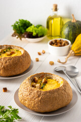 Pumpkin puree soup in a plate of bread, pumpkin soup with thyme , cheese and croutons on a white wooden background
