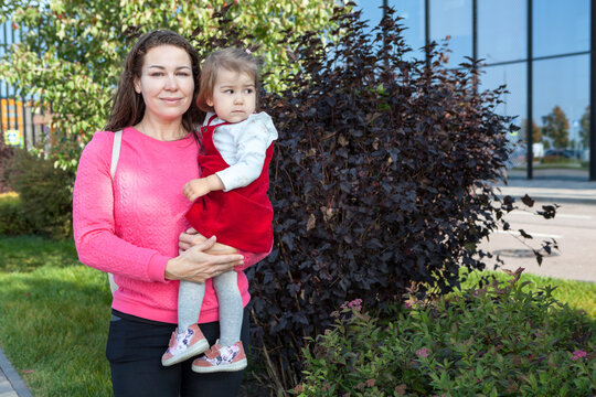 Portrait of mother holding the child in her arms, one year old daughter in red dress, copy space