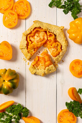 Pie with yellow tomatoes , bell peppers and sesame seeds, galette with vegetables and cheese on white wooden background, top view