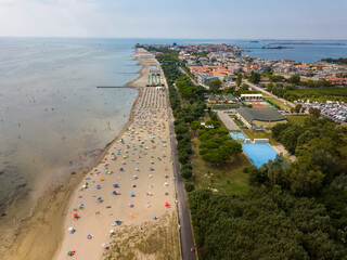 Aerial view of unidentifiable people enjoying summer at the beach of Grado in the province of Gorizia at the Northern Adriatic Sea. - obrazy, fototapety, plakaty