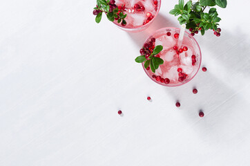 Autumn fresh fruit drink with red lingonberry, ice and straws in sunbeam on white wooden table, copy space, top view.
