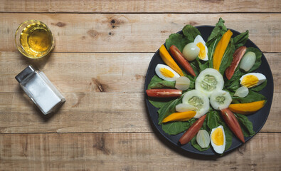 green leafy salad with eggs, tomatoes, cucumber, onions, mango, on a black plate.